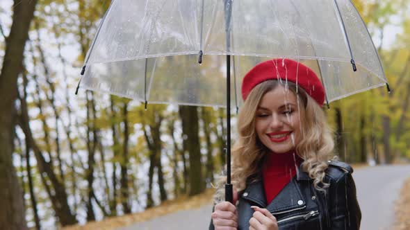 Smiling Happy Cheerful Woman in a Red Suit and a Biker Jacket with a Transparent Umbrella on a Rainy