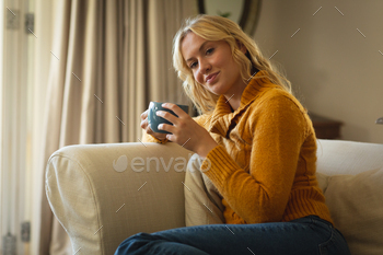Portrait of happy caucasian woman sitting on couch in living room holding coffee cup, smiling / Photodune, Misc