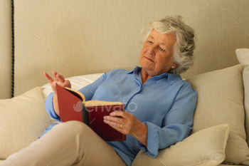 Senior caucasian woman sitting on bed and reading book in bedroom / Photodune, Misc