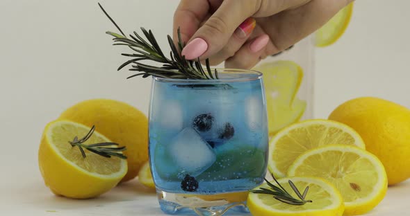 Adding Rosemary Branch in a Glass with Soda Lemonade Blue Cocktail