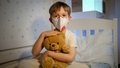 Cute little boy wearing protective medical mask holding and stroking his teddy bear in bed at night - PhotoDune Item for Sale