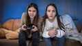 Two concentrated girls playing video games on game console in living room at night - PhotoDune Item for Sale