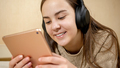 Smiling teenage girl with tablet computer lying on bed and listening music in headphones - PhotoDune Item for Sale