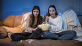 Two concentrated girls watching TV on sofa and eating popcorn from big bowl - PhotoDune Item for Sale