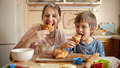 Happy smiling boy with mother covered in flour eating tasty croissant after baking at home. Children - PhotoDune Item for Sale