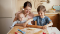 Young mother with little baby son looking at her older son rolling dough and cooking. Children - PhotoDune Item for Sale
