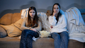 Two teenage girls watching TV on sofa and eating popcorn at night - PhotoDune Item for Sale