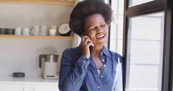 Happy african american woman talking on smartphone in kitchen