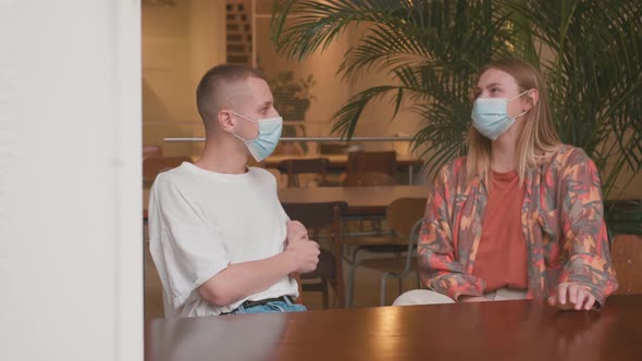 Man and Woman Sitting at a Cafe Table with Masks Talking and Two Cups of Coffee in Front