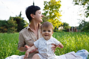 young mom hugs her little son while sitting in the park on the lawn / Photodune, Misc