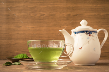 Glass cup of hot tea with green tea powder and teapot on the table. / Photodune, Misc