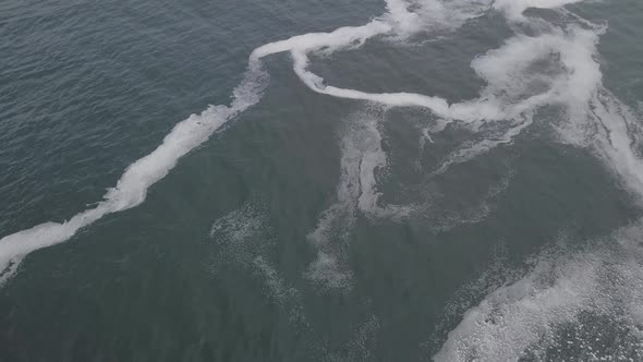 Slow aerial tilt from seafoam to horizon on misty, grey Indian Ocean