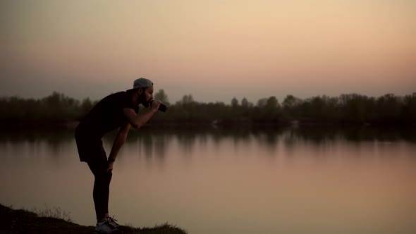 Tired Runner Drinking Water At Dusk. Triathlete Drinking Isotonic In Running Pause. Runner Relaxing.