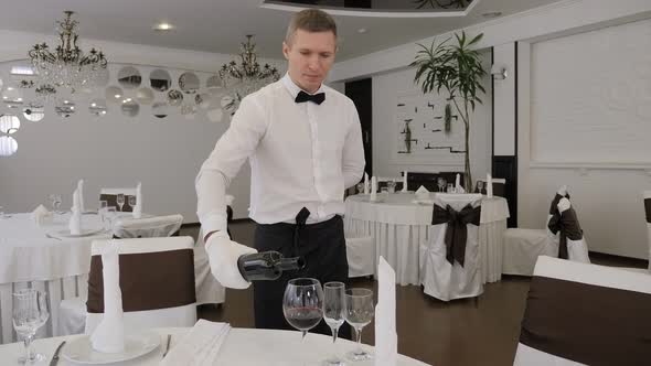 A Male Waiter Wearing White Gloves in a Restaurant Pours Red Wine Into a Glass