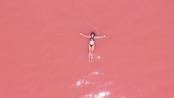 Aerial View of an Attractive Woman in a Bikini Floating in Pink Salt Lake