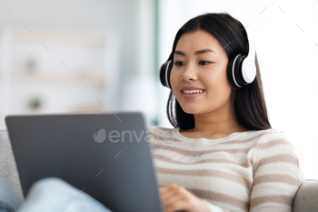 With Laptop At Home, Millennial Korean Woman Wearing Headphones Watching Webinar On PC Computer, Enjoying Distance Learning, Closeup Shot