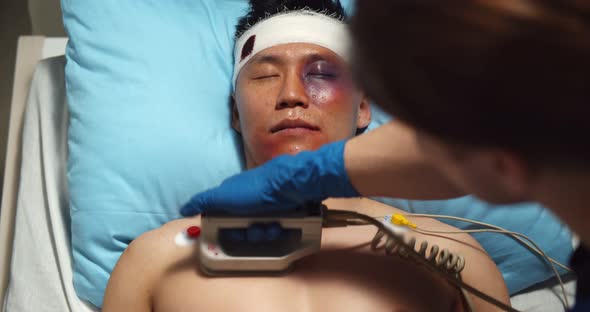 Close Up of Doctor Using Defibrillator on Injured Asian Male Patient in Ward at Hospital