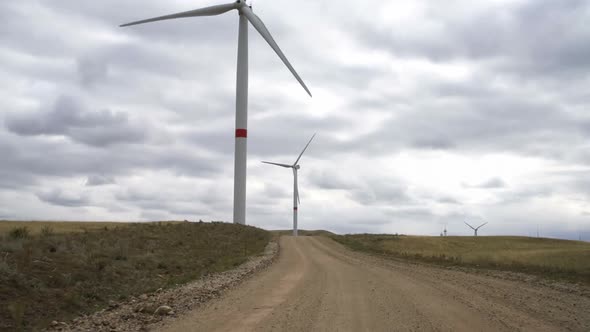 Motion the Blades of a Large Wind Turbine in a Field Against a Background of Cloudy Blue Sky Near