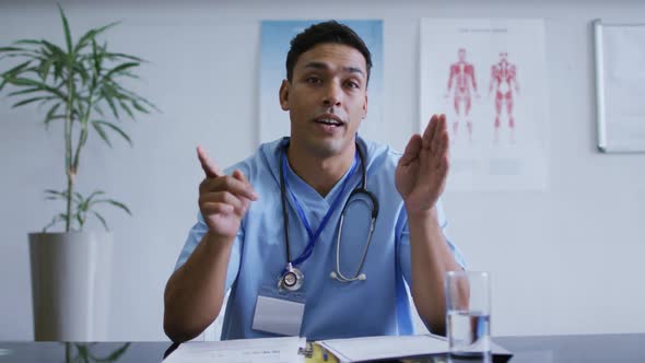 Mixed race male doctor at desk talking and gesturing during video call consultation