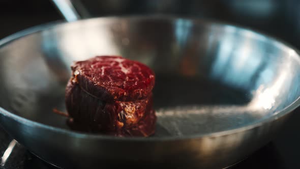 Close-up of a raw filet mignon being cooked in a frying pan