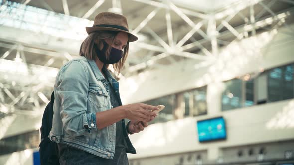 Woman in a Protective Mask Standing at the Airport and Using Her Smartphone