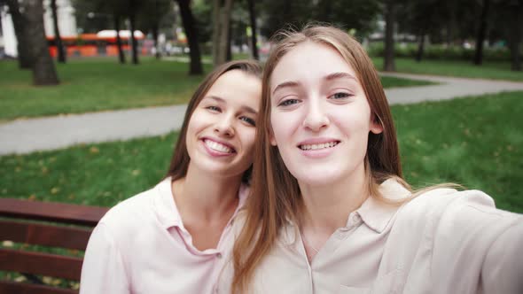 POV shot of young girls couple making video call sitting on bench in the street.