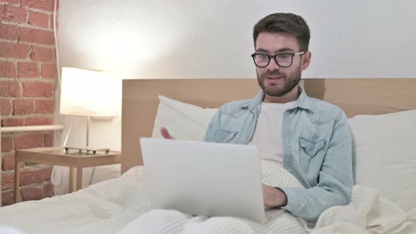 Young Male Designer Doing Video Chat on Laptop in Bed