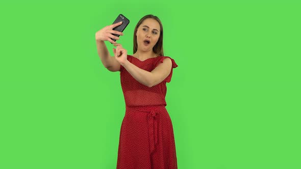 Tender Girl in Red Dress Is Making Selfie on Mobile Phone Then Looking Photos. Green Screen