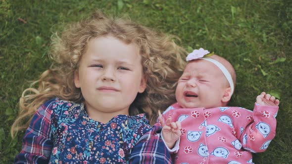 A Little Girl Kisses Her Baby Sister in the Garden on the Grass