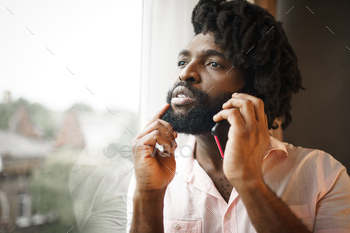 Close up photo of a black man in formal shirt talking on his phone near the window / Photodune, Misc