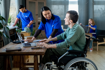 Asian woman in volunteer t-shirt helping disabled man / Photodune, Misc