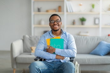 Positive disabled black in wheelchair holding notebooks and smiling at camera at home / Photodune, Misc