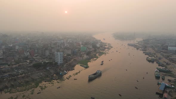 River through city with cargo ship and buildings - aerial establishing shot with rising sun in foggy