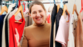 Beautiful smiling woman behind long rack of clothes on hangers choosing dress to wear - PhotoDune Item for Sale