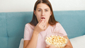 Portrait of young woman wearing pajamas watching television on bed on weekend and eating popcorn - PhotoDune Item for Sale