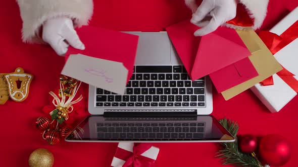 Top View Santa Hands in White Gloves Are Typing on Keyboard Laptop By Red New Year Decorated Table