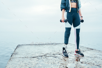 Woman in sports clothing with prosthetic leg holding dumbbells / Photodune, Misc