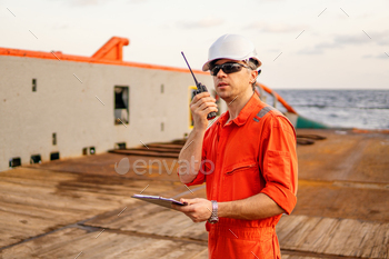Deck Officer on deck of offshore vessel holds VHF walkie-talkie radio / Photodune, Misc