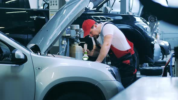 Auto Mechanic Using Flashlight to Check the Insides of a Car