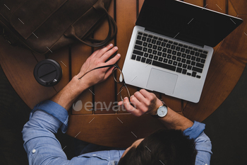 overhead view of man using laptop with website while sitting at table with coffee and notepad / Photodune, Misc