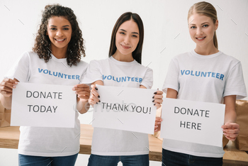 multiethnic female volunteers holding charity placards and looking at camera / Photodune, Misc