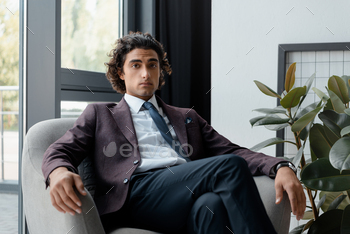 portrait of confident businessman in suit sitting in armchair and looking at camera in office / Photodune, Misc