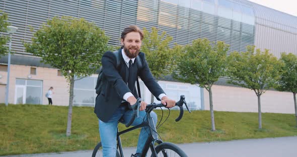 Man in Stylish Clothes Sitting on His Bike and Looking at Camera Near Modern Big Urban Building