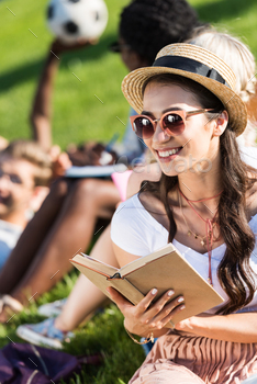 smiling asian girl in sunglasses and straw hat reading book in park / Photodune, Misc