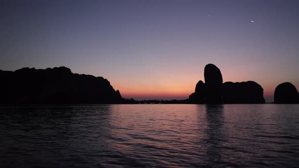 boat motoring on the glassy water during an orange morning sunrise in Krabi Thailand with limestone