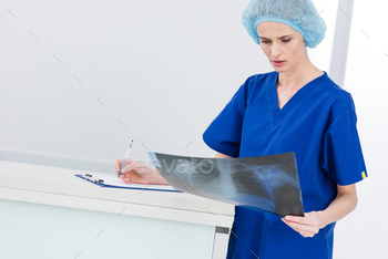 female surgeon in medical cap looking at x-ray and writing diagnosis in hospital / Photodune, Misc