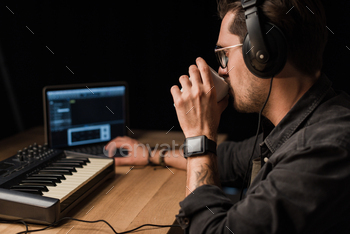 musician working with keyboard controller in dark room and drinking coffee / Photodune, Misc