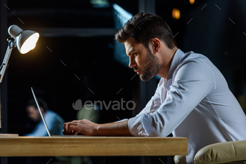 side view of businessman working at laptop in the evening / Photodune, Misc