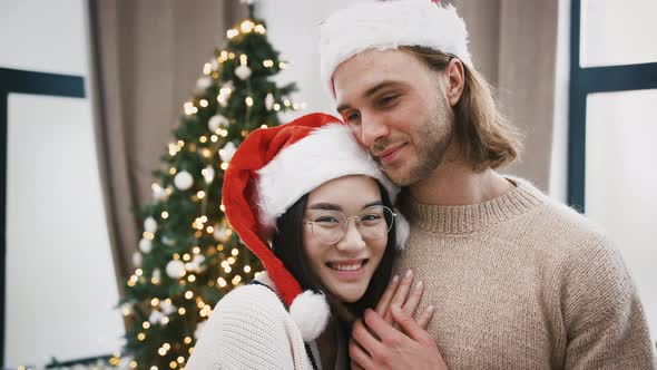 Loving Mixed Race Pair Smiling and Hugging Each Other Standing at Home Against Green Decorated