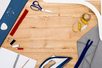 top view of iron, zippers, notebook with pencil and other tailoring equipment on wooden table / Photodune, Misc
